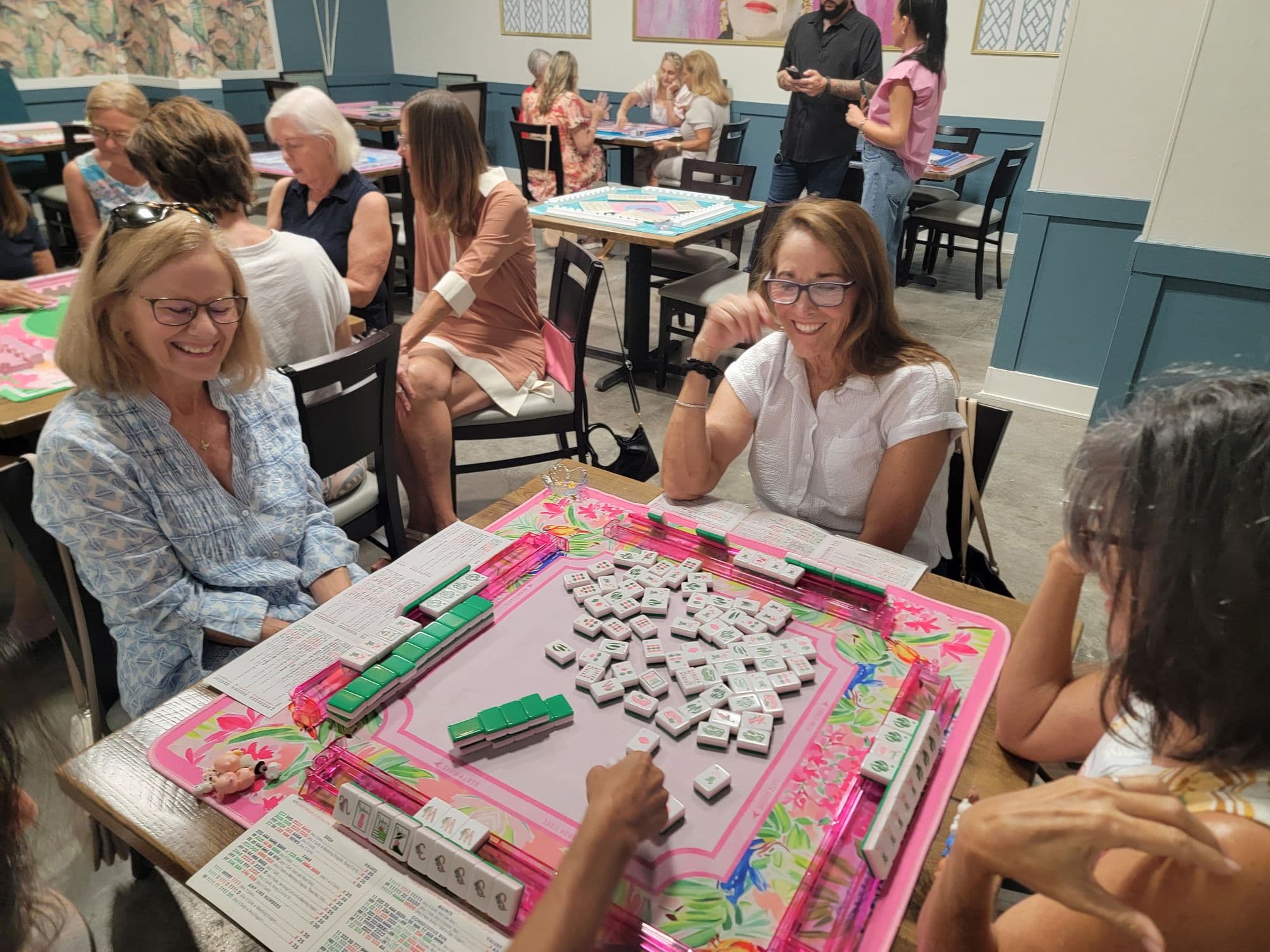 Friends laughing over a game of mahjong at pink tables inside the Sparrow & Palm clubhouse